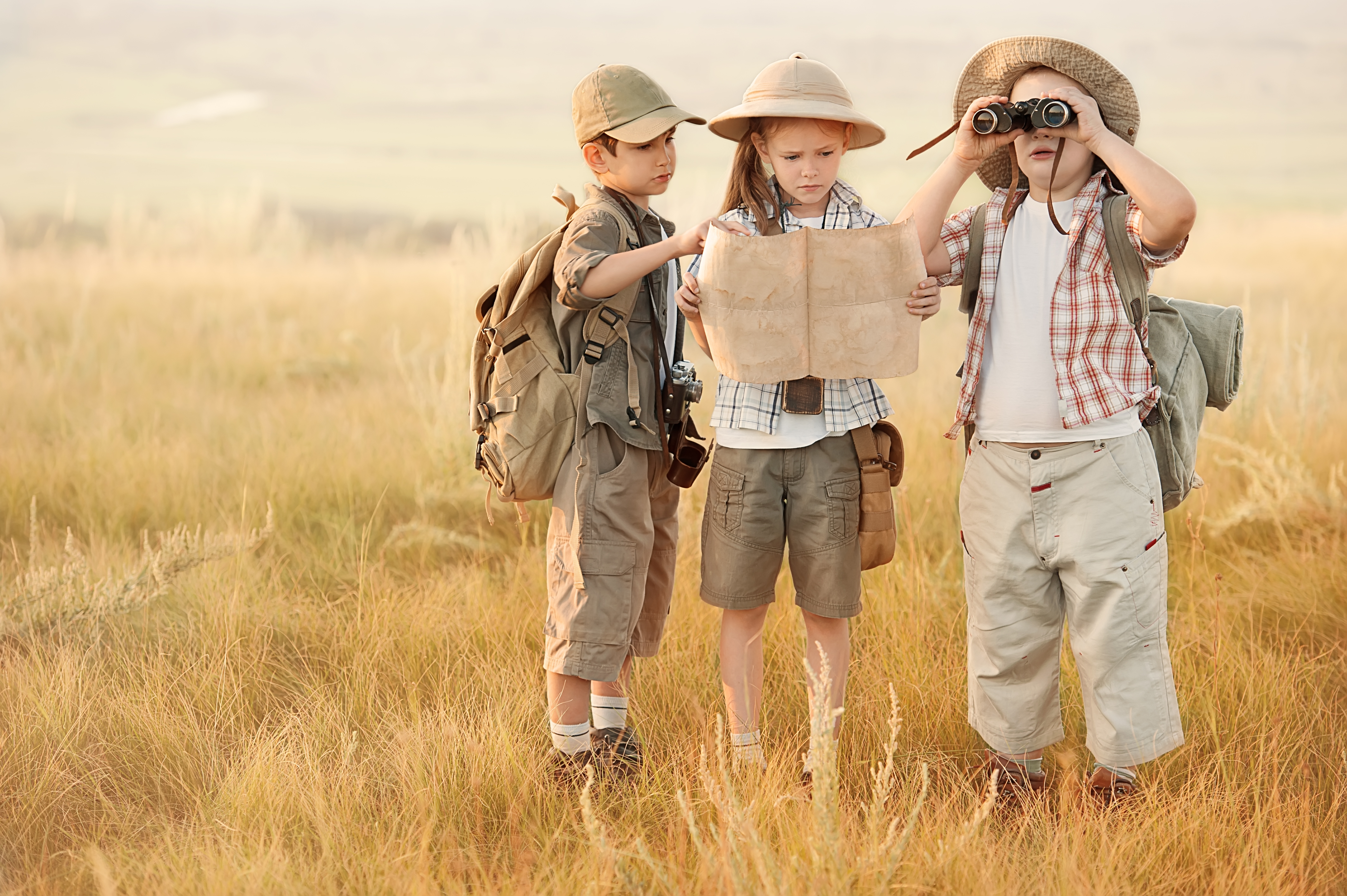 Three,children,with,maps,and,travel,backpacks,on,steppe,valleys